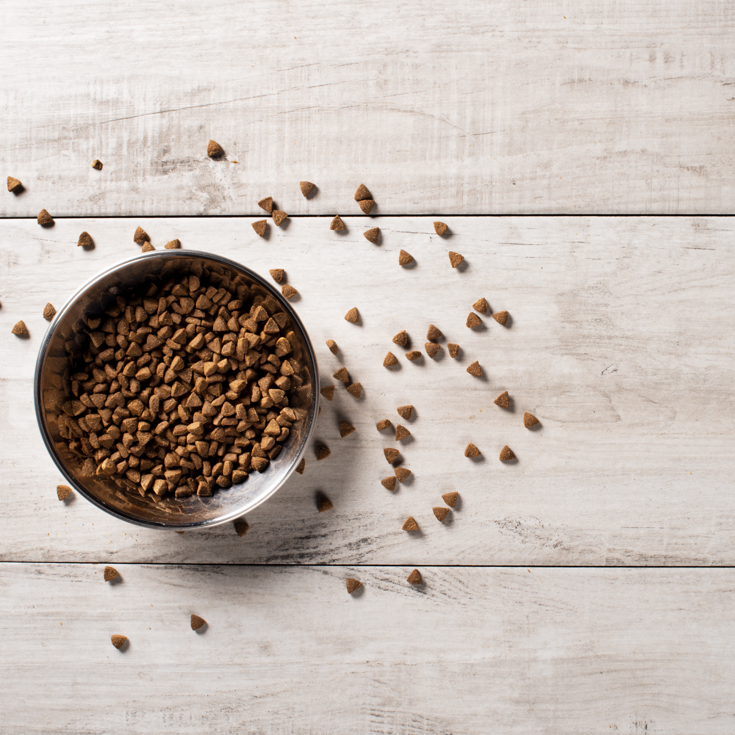 Cat kibble in a bowl and spilling onto a wooden background