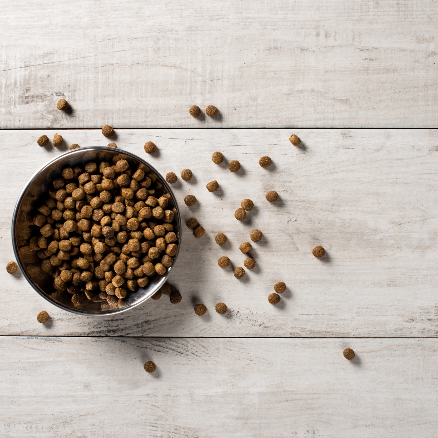Lamb and rice dog kibble spilling out of a bowl onto a wooden background