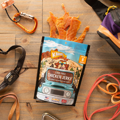 Chicken jerky against a wooden background with adventure gear around it, highlighting that these treats are meant for adventure