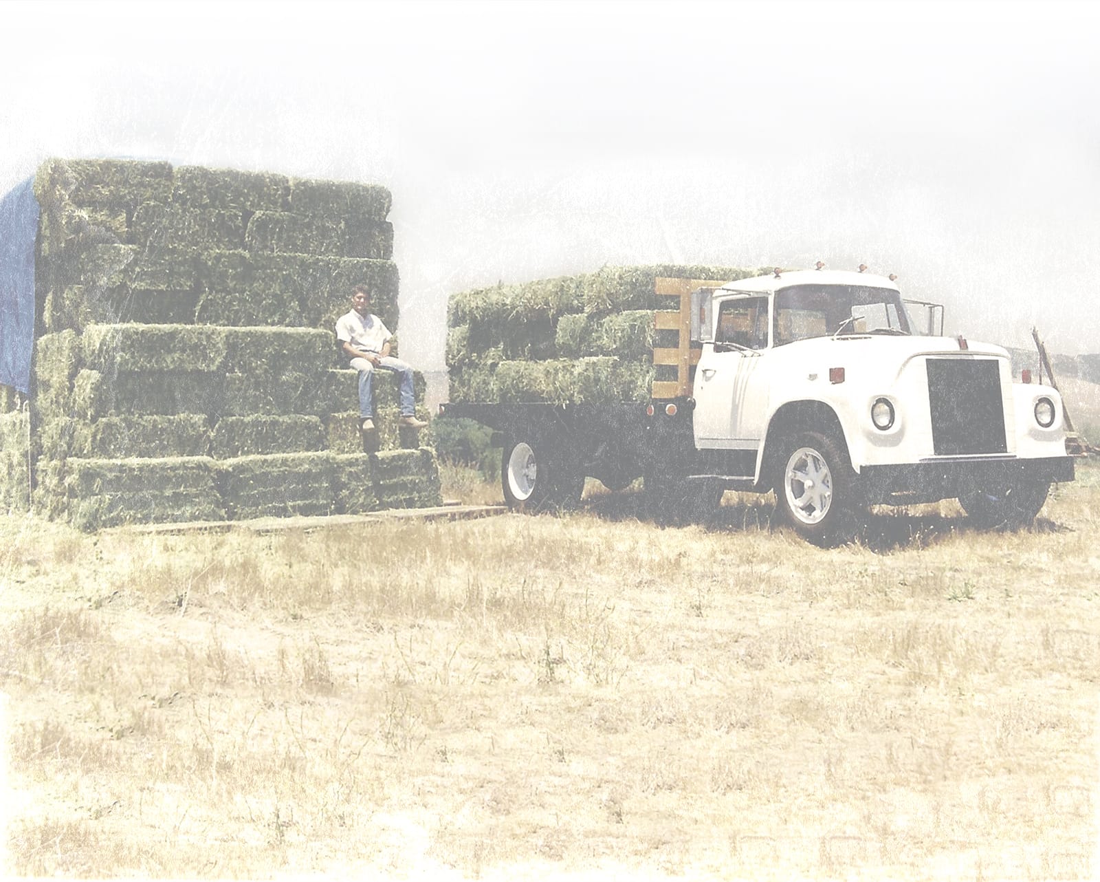 Mike sitting on a stack of hay next to a loaded pickup truck